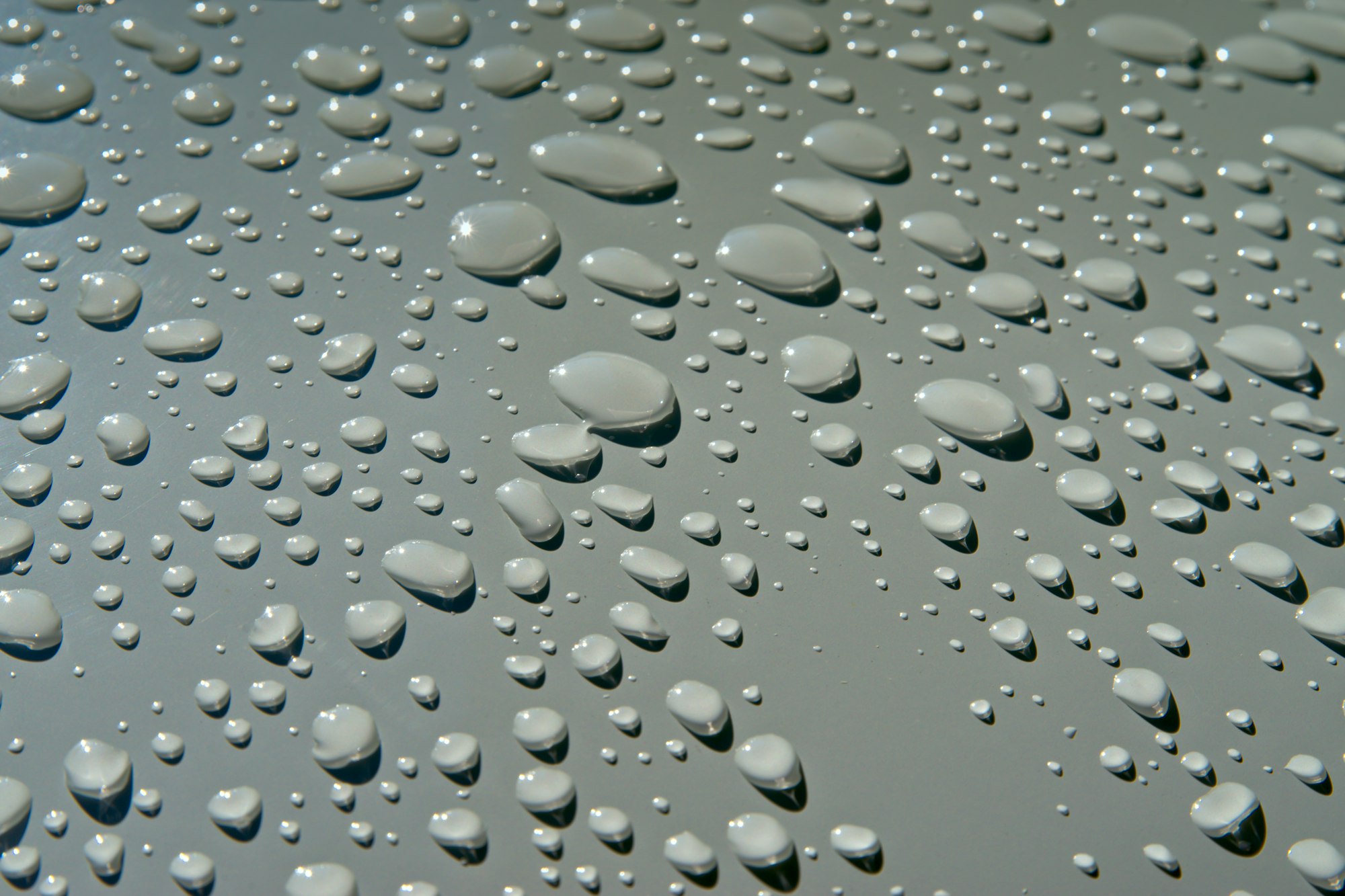 Close-up of fresh water droplets beaded on a smooth neutral surface, catching the light.